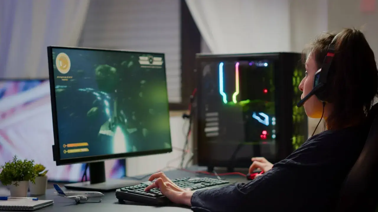 Graczka w słuchawkach gra w grę FPS, co to za gatunek? Komputer z kolorowym podświetleniem.