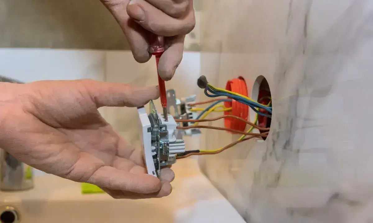 Elektryk dokonuje podłączenia gniazda, używając śrubokręta do połączenia 4 przewodów.