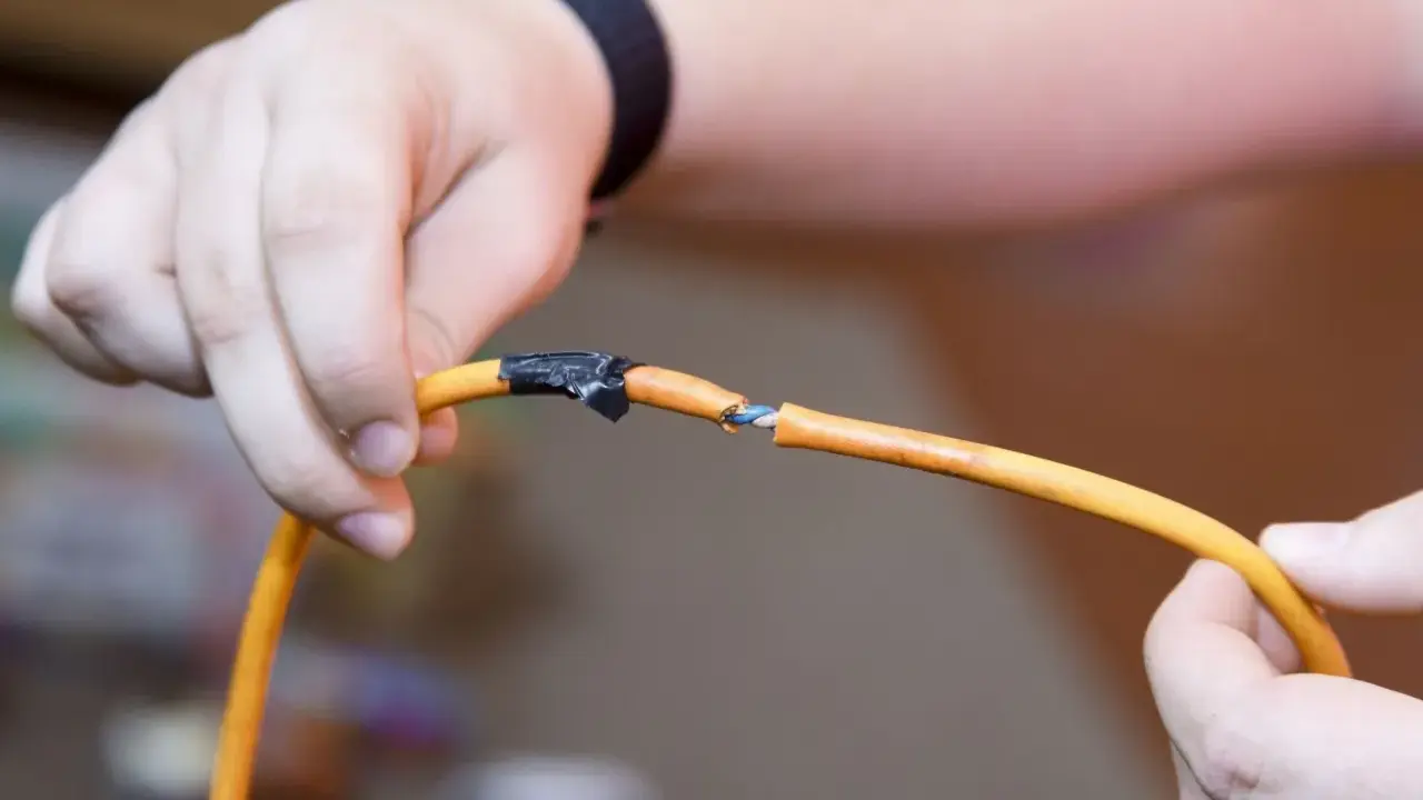 Dłonie trzymają przecięty pomarańczowy kabel, odsłaniając niebieskie żyły. Pokazuje to, jak połączyć przecięty kabel w ścianie.