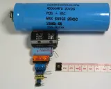 Różne kondensatory elektrolityczne, od dużego niebieskiego po małe czarne i kolorowe, ułożone obok miarki. Budowa kondensatora elektrolitycznego jest tu widoczna w całej okazałości.