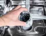 Ręka wyjmuje filtr zmywarki. Może to być przyczyną, że zmywarka nie domywa naczyń.