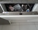 Pierwsze uruchomienie zmywarki Bosch. W koszu różowy kubek, biała miseczka i metalowy garnek. Na panelu przycisk "start".