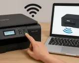 Ręka naciska przycisk "GX" na drukarce Brother, pokazując, jak podłączyć drukarkę do wifi. Na ekranie laptopa widoczny jest schemat połączenia.