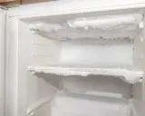W lodówce widać jabłko, banana i jogurty. Na ściankach pojawia się szron, a w rogu widać zielony odpływ.