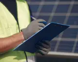 Technik w kamizelce odblaskowej notuje powody, **dlaczego fotowoltaika się wyłącza**, przy panelach słonecznych.