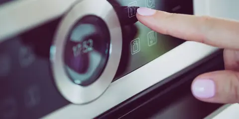 Palec naciska ikonę widelca i noża na panelu piekarnika Samsung Dual Cook. Widoczne symbole na piekarniku Samsung Dual Cook.