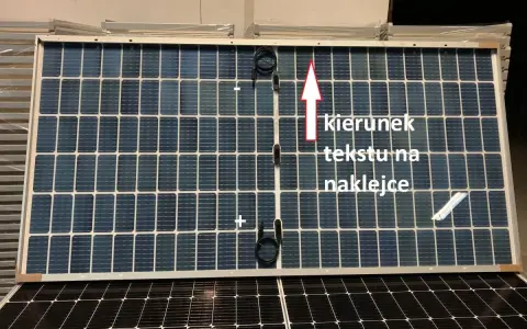 Panel fotowoltaiczny z oznaczeniami plus i minus. Strzałka wskazuje kierunek tekstu na naklejce.