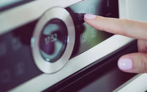 Palec naciska ikonę widelca i noża na panelu piekarnika Samsung Dual Cook. Widoczne symbole na piekarniku Samsung Dual Cook.