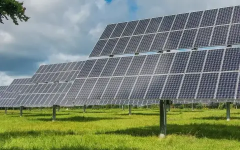 Rzędy paneli fotowoltaicznych tworzą farmę fotowoltaiczną 1 MW, która czerpie energię ze słońca na zielonej łące.