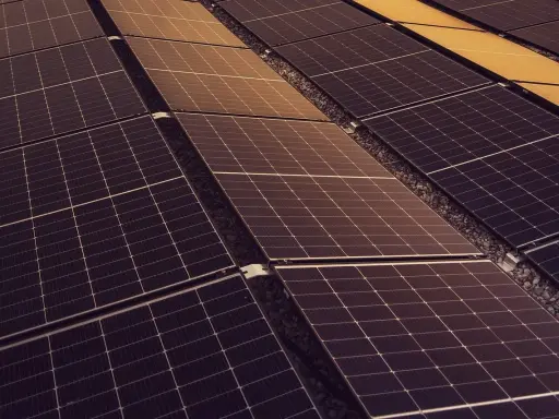 Rzędy paneli fotowoltaicznych, których sprawność zależy od nasłonecznienia. Widoczne są ciemne i lekko złote odcienie.