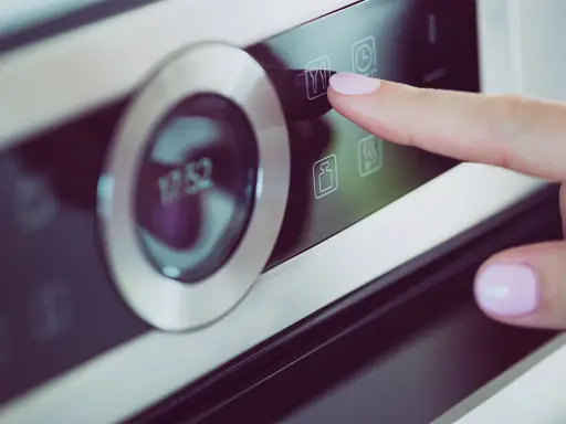 Palec naciska ikonę widelca i noża na panelu piekarnika Samsung Dual Cook. Widoczne symbole na piekarniku Samsung Dual Cook.