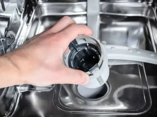 Ręka wyjmuje filtr zmywarki. Może to być przyczyną, że zmywarka nie domywa naczyń.