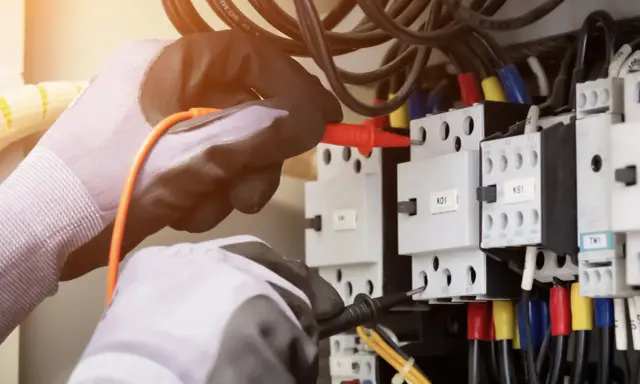 Elektryk w rękawicach sprawdza instalację, by dowiedzieć się, jak sprawdzić moc przyłączeniową.