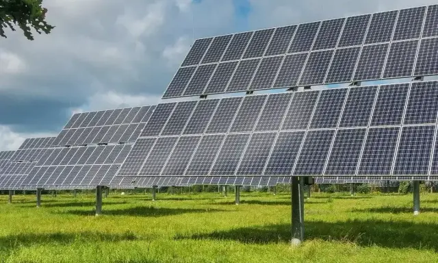 Rzędy paneli fotowoltaicznych tworzą farmę fotowoltaiczną 1 MW, która czerpie energię ze słońca na zielonej łące.