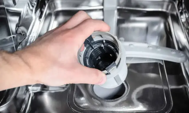 Ręka wyjmuje filtr zmywarki. Może to być przyczyną, że zmywarka nie domywa naczyń.