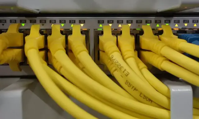 Żółte kable RJ45 podłączone do portów sieciowych, z podświetlonymi diodami. Kolejność portów od 24 do 43.
