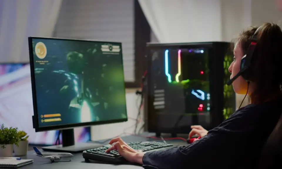 Graczka w słuchawkach gra w grę FPS, co to za gatunek? Komputer z kolorowym podświetleniem.