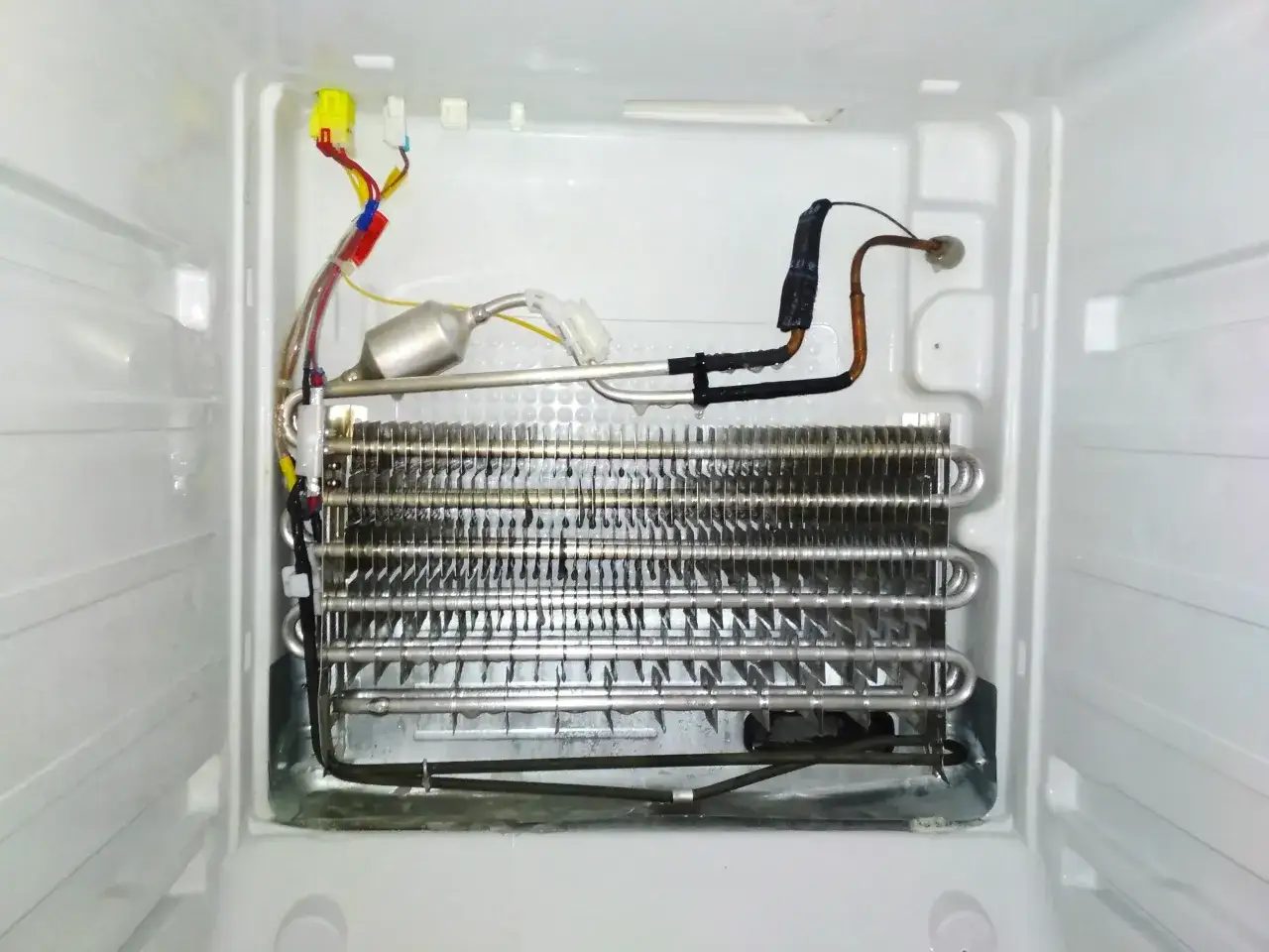 Wnętrze lod&oacute;wki z widocznym parownikiem i elementami elektrycznymi. Może to być przyczyną, że lod&oacute;wka słabo chłodzi.