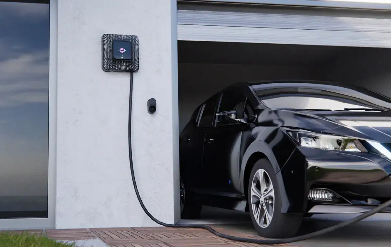 Czarny samoch&oacute;d elektryczny podłączony do ładowarki ściennej. Czas ładowania samochodu elektrycznego w domu jest wygodny dzięki tej stacji.