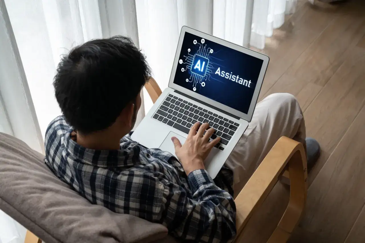 Mężczyzna siedzi na krześle i korzysta z laptopa, na kt&oacute;rego ekranie widnieje napis 