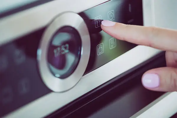 Palec naciska ikonę widelca i noża na panelu piekarnika Samsung Dual Cook. Widoczne symbole na piekarniku Samsung Dual Cook.